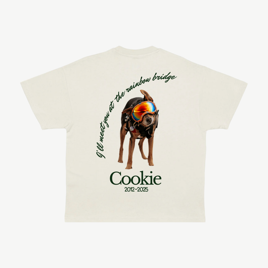 Back of a cream tee with Cookie’s portrait wearing colourful goggles, the dates 2012–2025, and Rainbow Bridge memorial lettering.